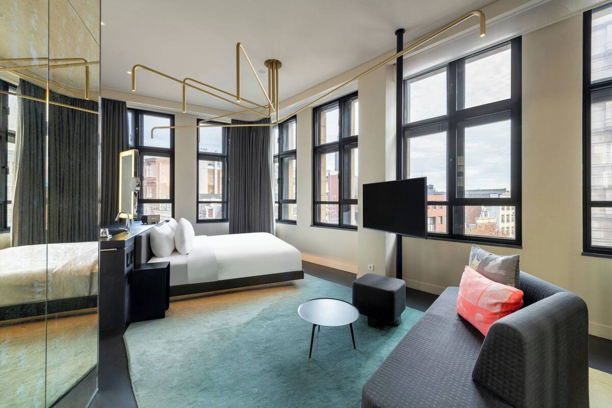 A modern hotel room with a large bed, a sofa, a small round table, and a TV.