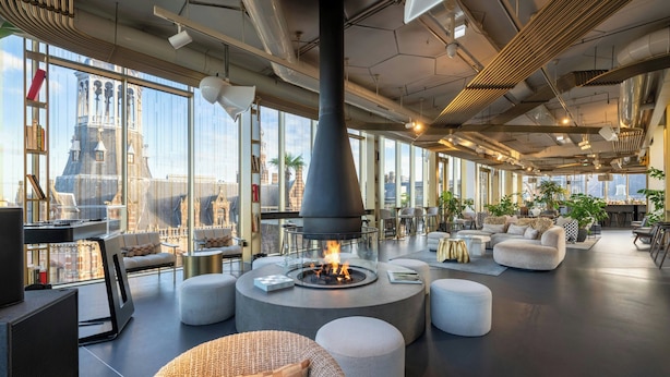 Ein stilvoller Lounge-Bereich mit einem zentralen Kamin, bequemen Sitzgelegenheiten und großen Fenstern mit Blick auf die Stadt.