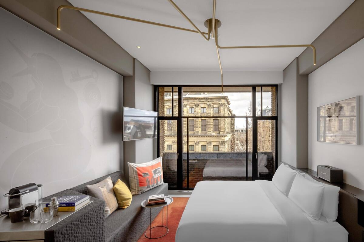 A modern hotel room with a large bed, a sofa, a small table, and a TV.