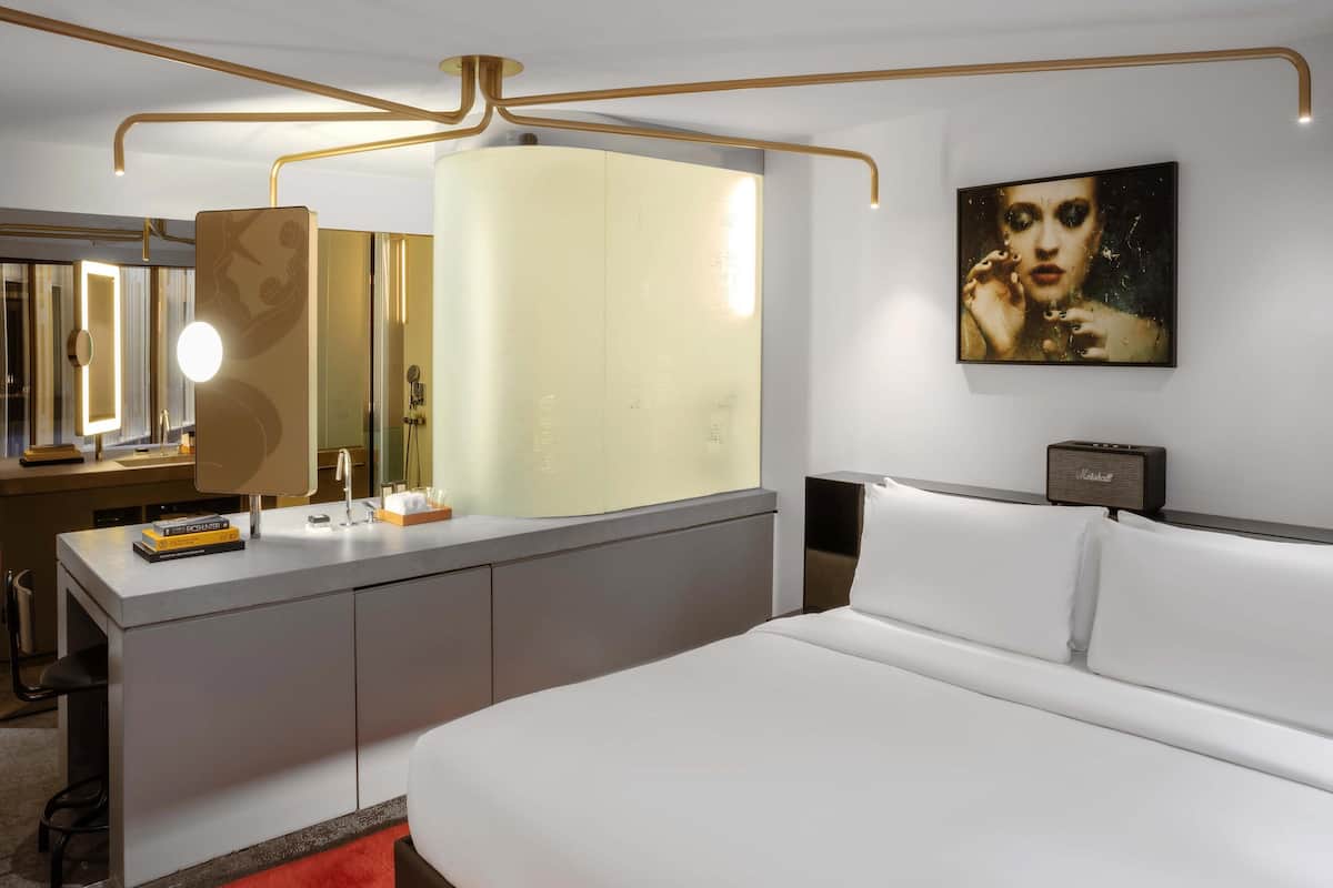 A modern hotel room with a large bed, a vanity with a mirror, and a painting on the wall.
