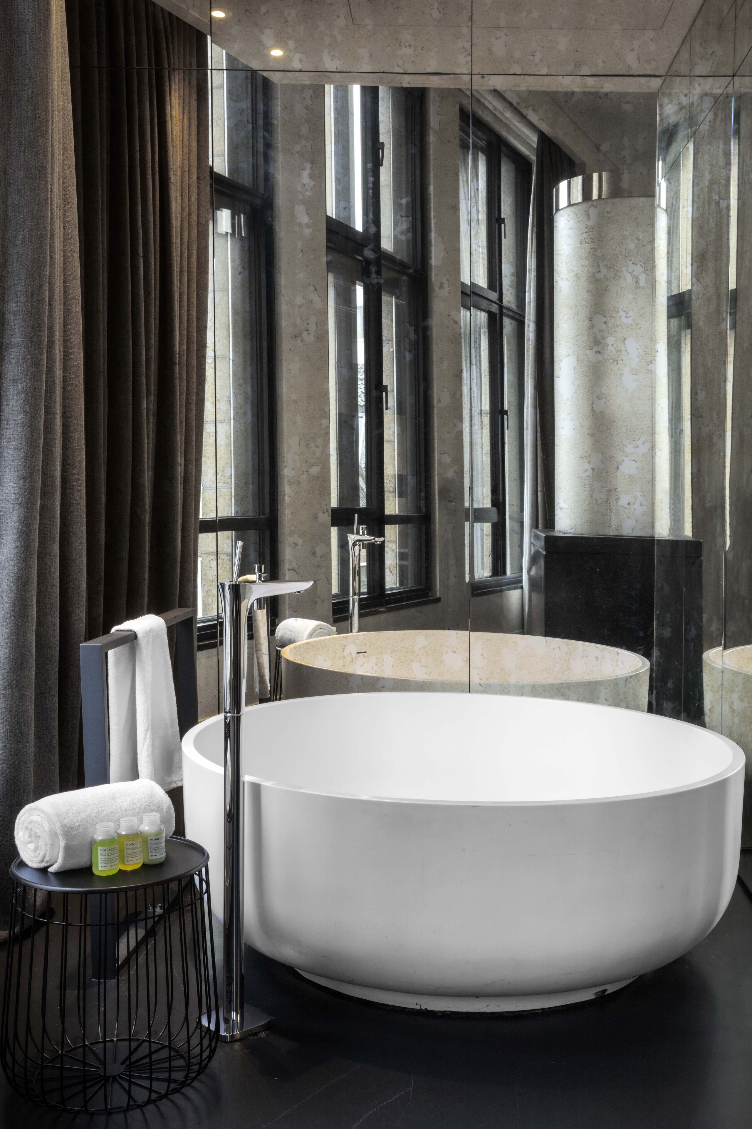 Une salle de bain moderne avec une grande baignoire sur pieds, un miroir rond et une petite table ronde sur laquelle sont posés des articles de toilette.