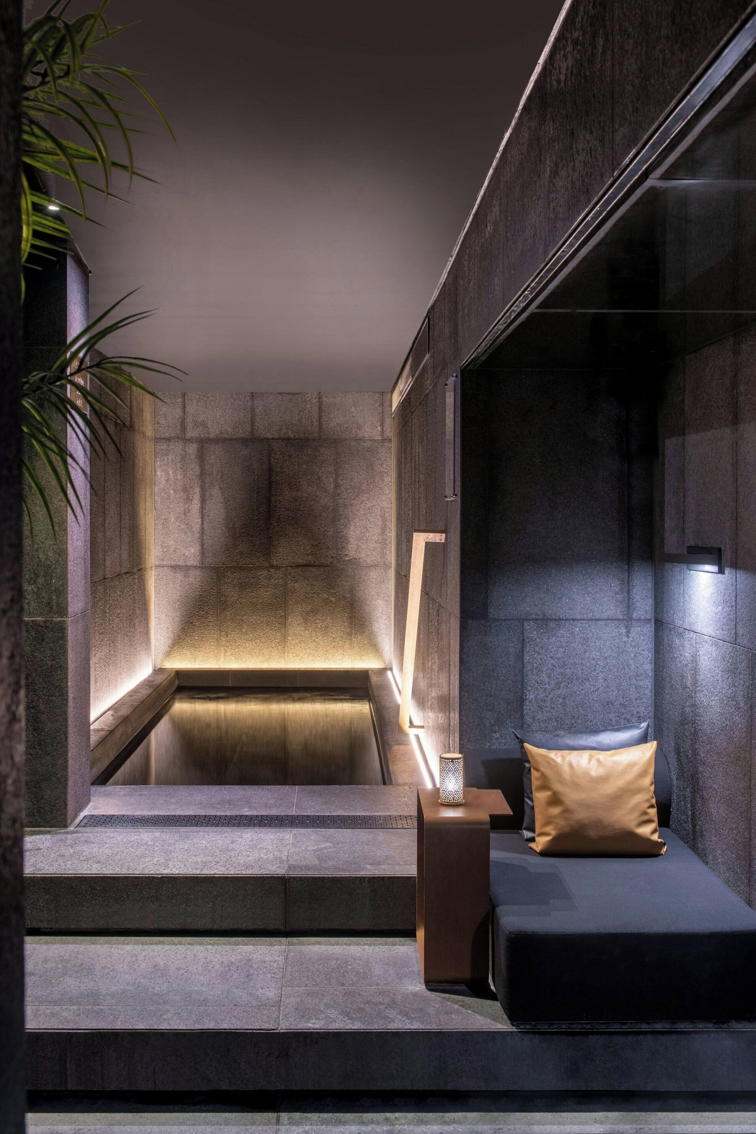 Un baño moderno con pared de piedra, un banco empotrado y una pequeña mesa con lámpara.