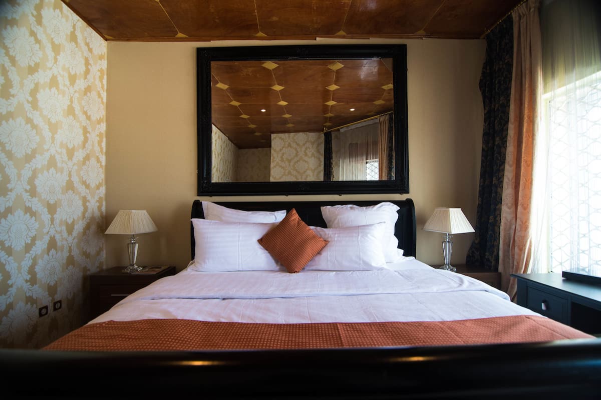 A hotel room with a large bed, two bedside tables, a mirror above the bed, and a window with curtains.