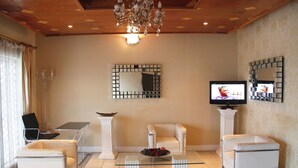 Uma sala de estar com uma mesa de centro de vidro, duas poltronas brancas, uma televisão e espelhos decorativos nas paredes.