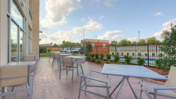 Une terrasse extérieure avec des tables et des chaises, donnant sur un parking, et un bâtiment visible à l’arrière-plan.