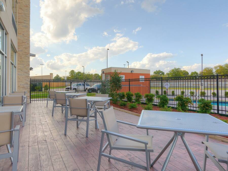 An outdoor patio with tables and chairs, a view of a parking lot, and a building in the background.