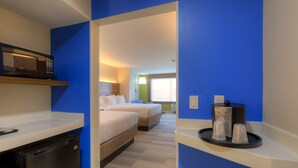 Camera d'albergo con angolo cottura, due letti, un'ampia finestra e un vassoio con tazze e una bottiglia.