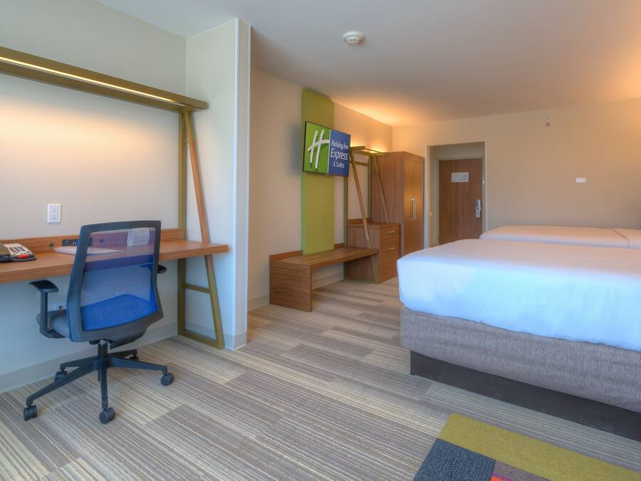 A hotel room with a desk, office chair, bed, and a TV on the wall.