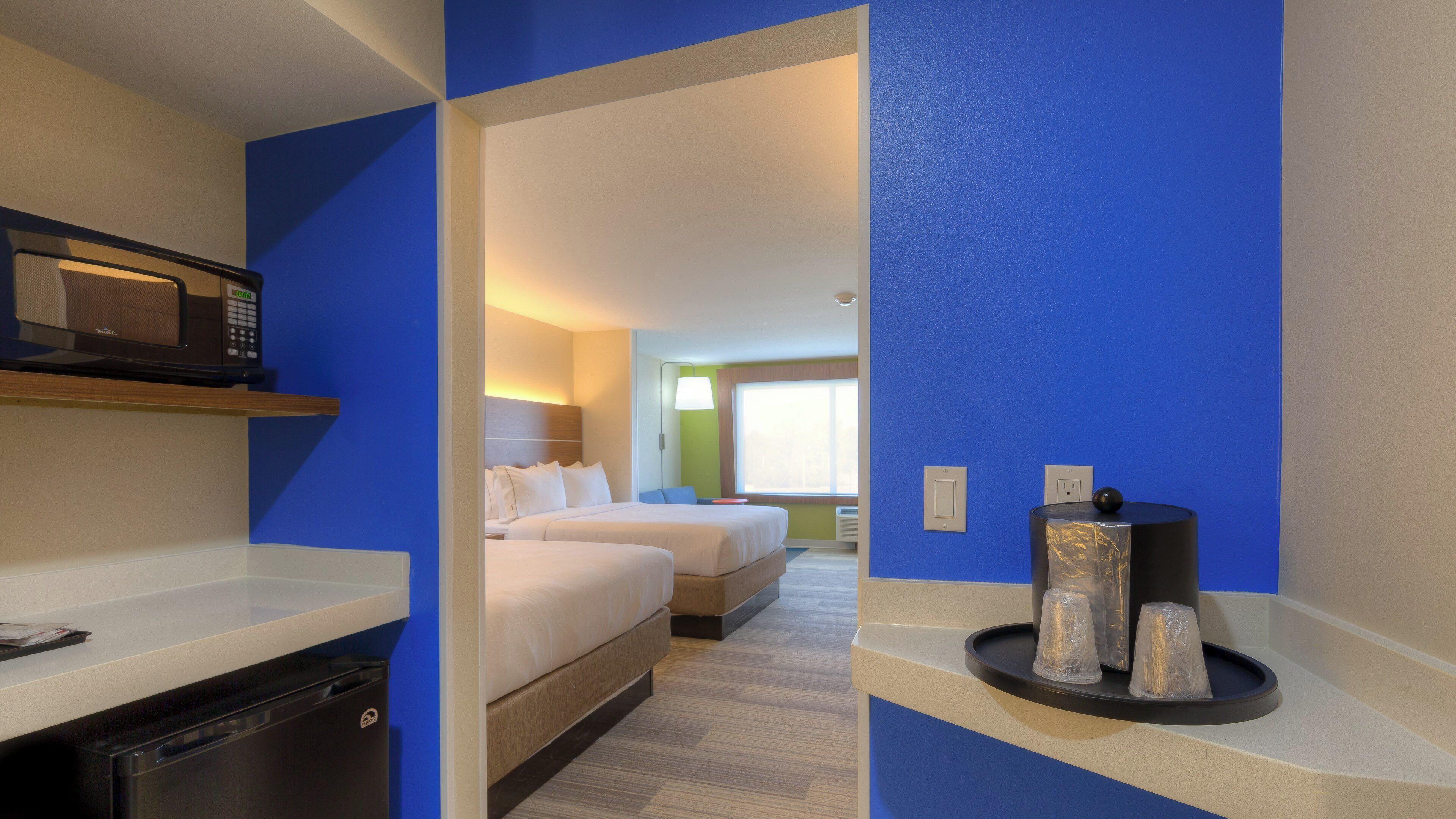 Habitación de hotel con microondas, cama, mesita de noche y bandeja con tazas.