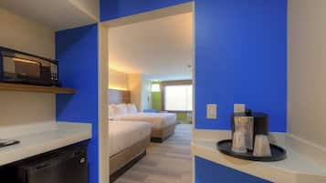 Habitación de hotel con microondas, cama, mesita de noche y bandeja con tazas.