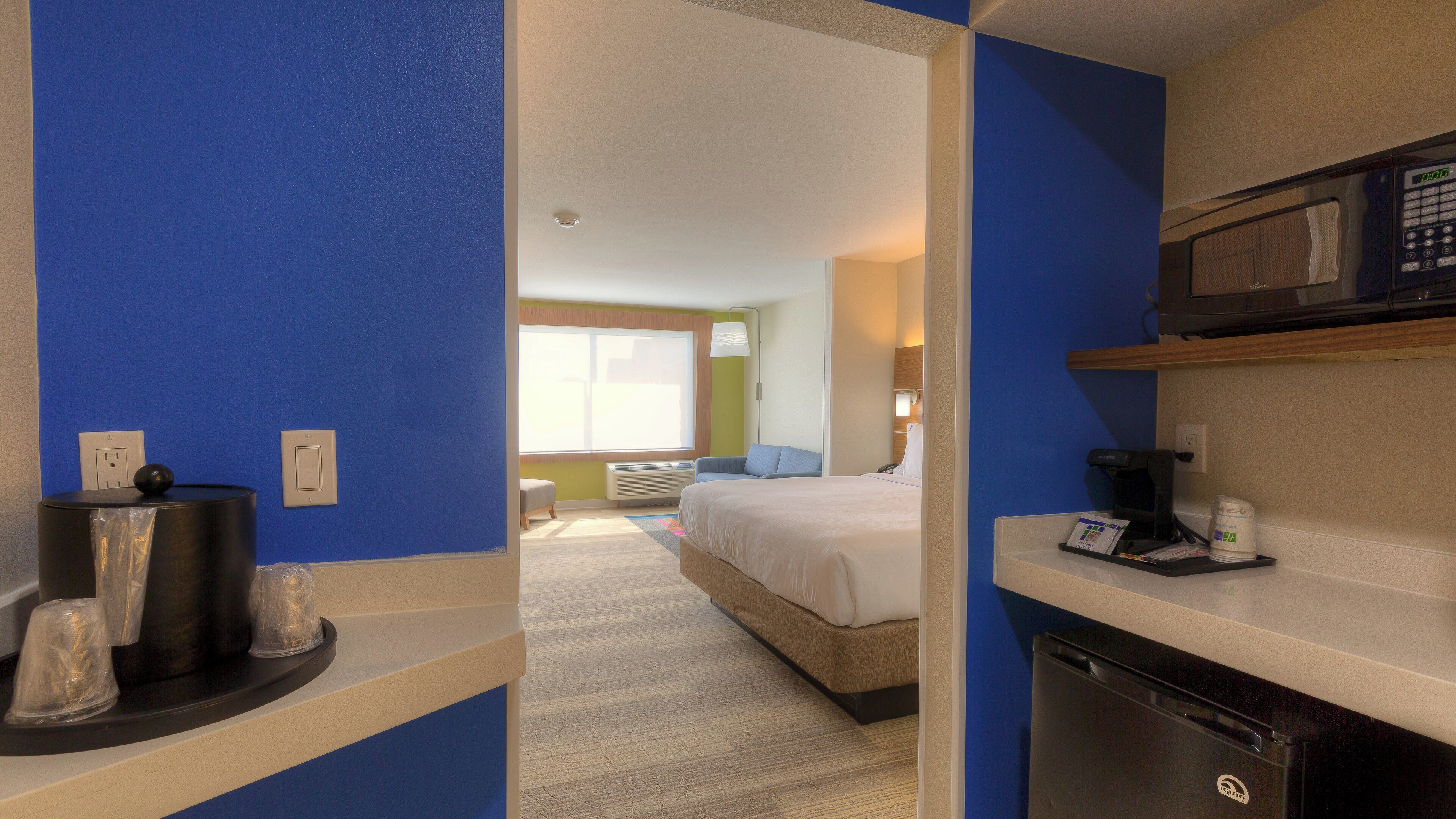 A hotel room with a bed, a desk with a microwave, a coffee maker, and a trash bin.