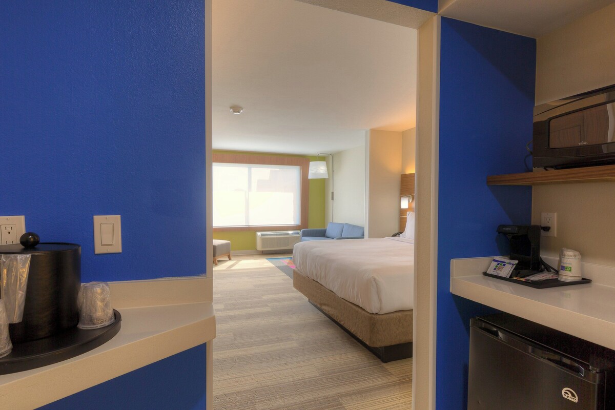 A hotel room with a bed, a desk with a microwave, a coffee maker, and a trash bin.
