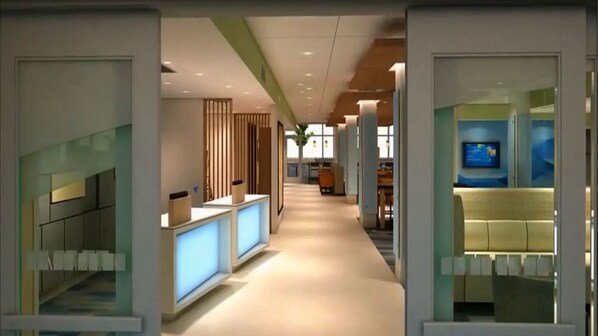A modern hotel corridor with reception desks, a seating area, and a television screen. - Holiday Inn Express & Suites Tulsa Midtown by IHG (Tulsa)