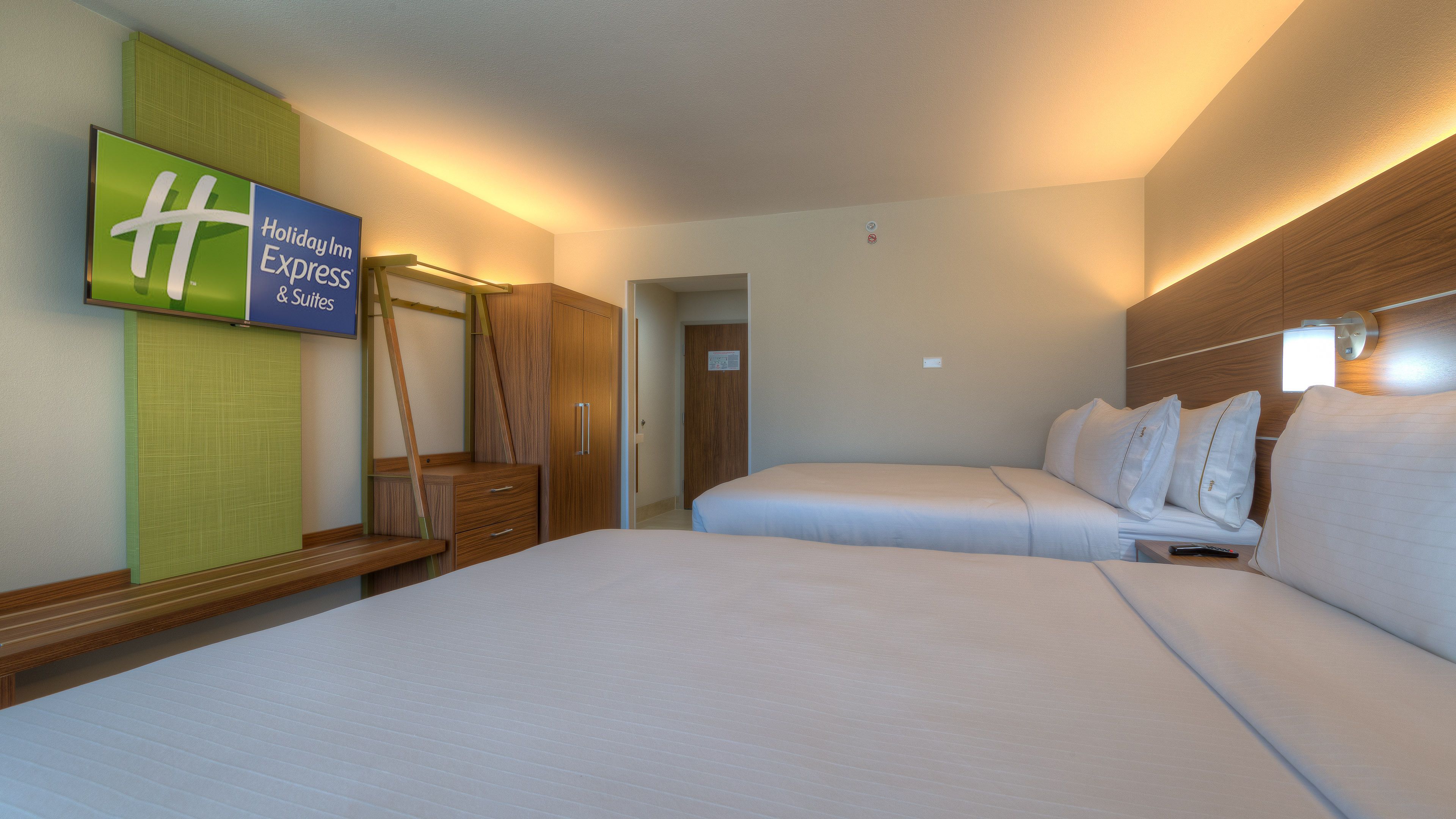 A hotel room with two beds, a flat-screen TV, a wooden wardrobe, and a mirror.