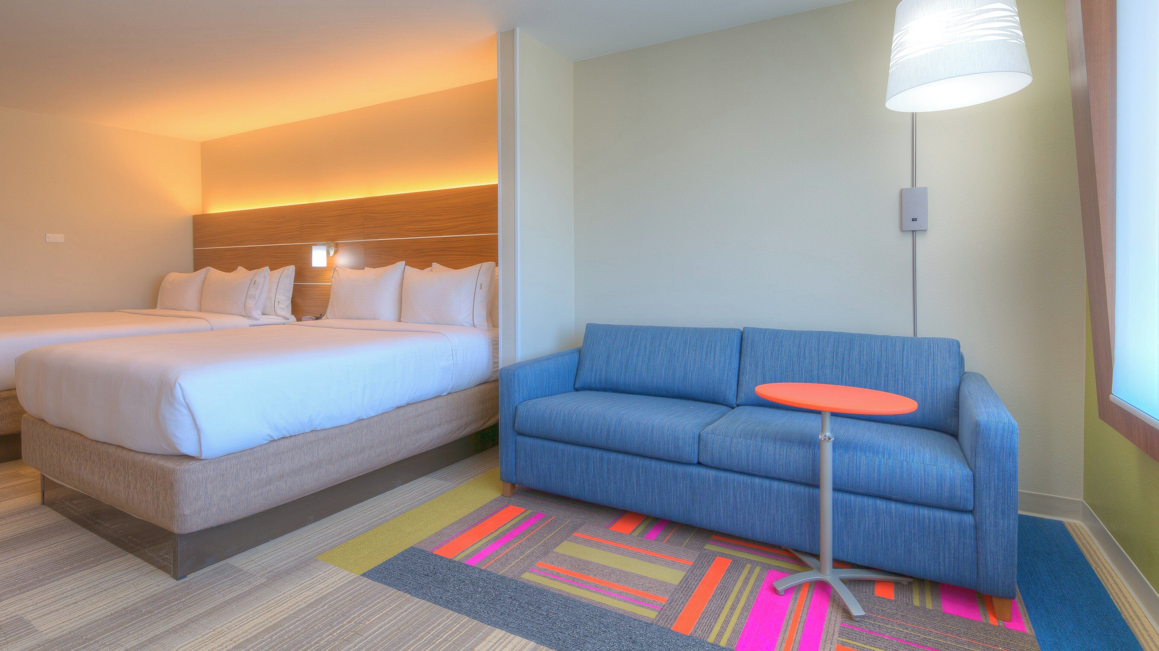 A hotel room with two beds, a blue sofa, a small orange table, and a colorful striped rug.