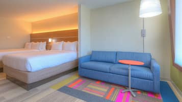 A hotel room with two beds, a blue sofa, a small orange table, and a colorful striped rug.