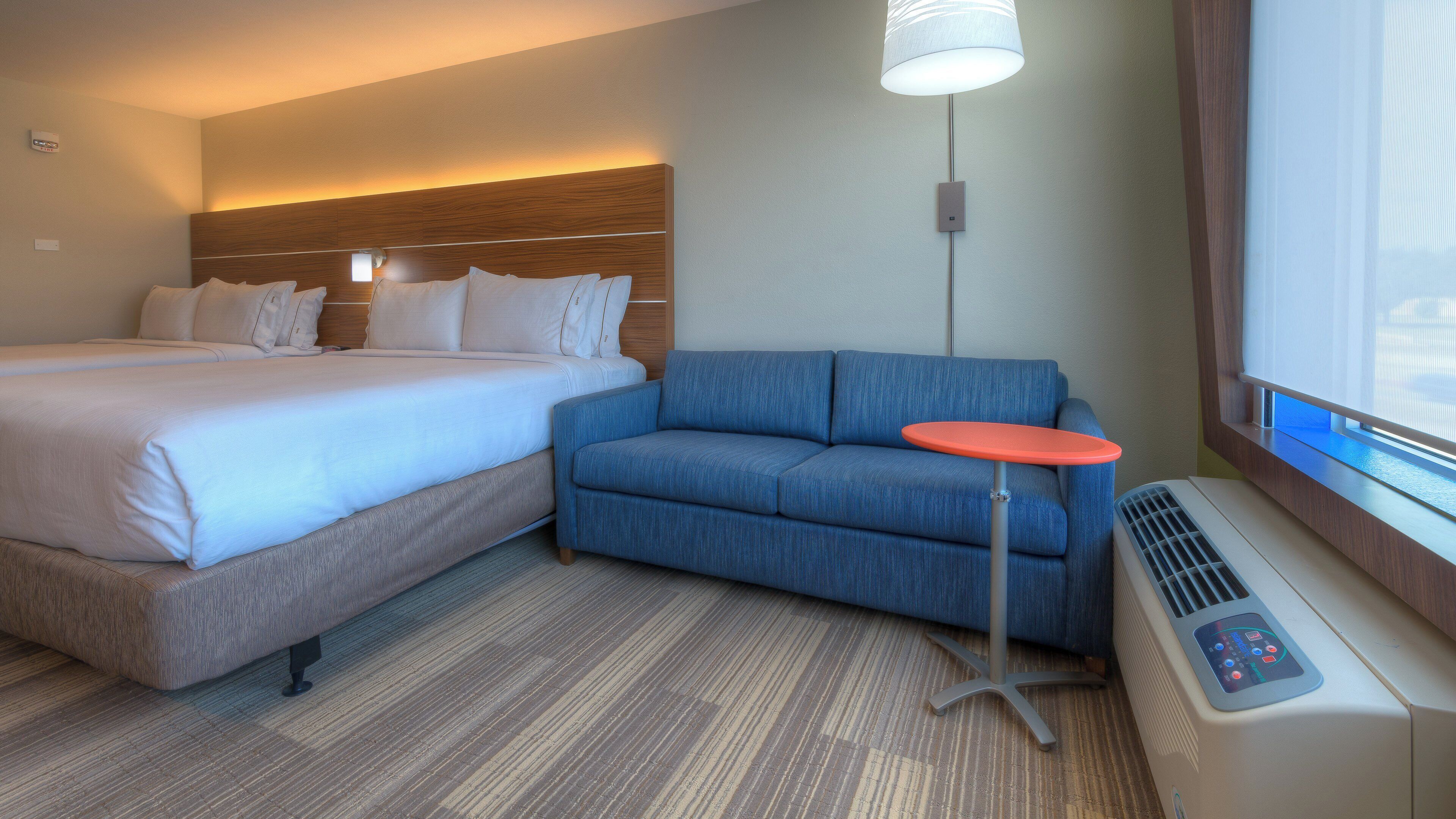 A hotel room with a bed, a sofa, a small table, and a heater.