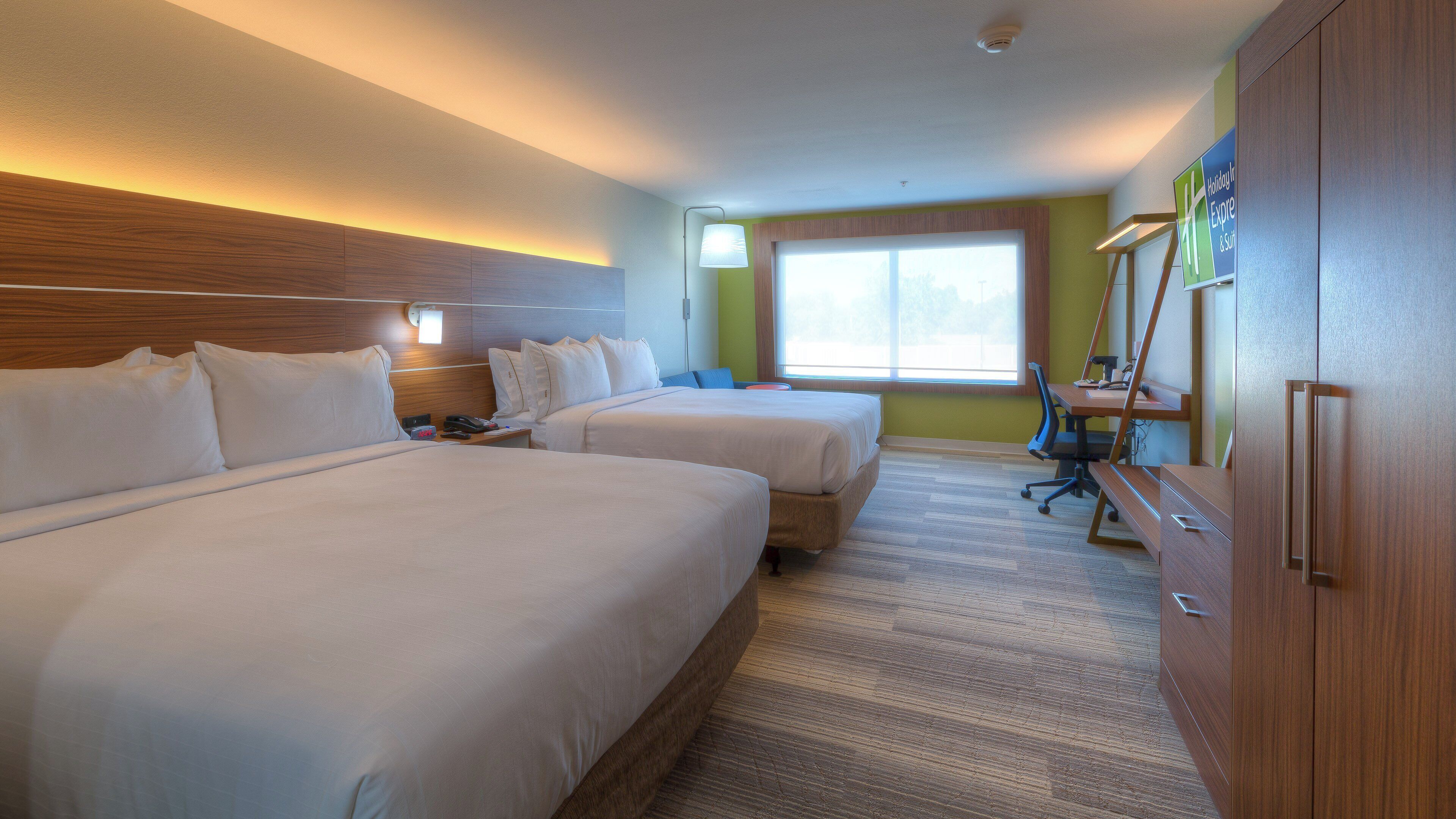 A hotel room with two beds, a desk, a chair, and a large window.