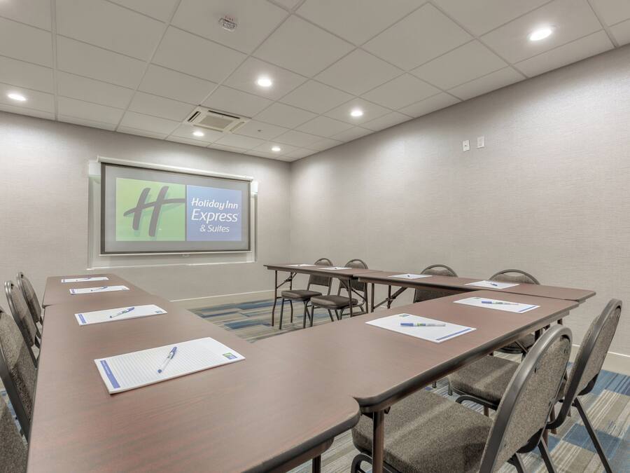 A conference room with a long table, chairs, a projector screen displaying 'Holiday Inn Express & Suites', and a fire alarm on the ceiling.