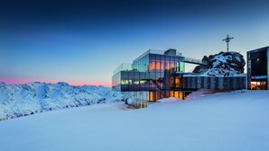 A modern glass building with a ski lift and a cross on a mountain peak. - Ötztal Chalet (Sautens)