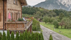A wooden chalet with a balcony, a mountain backdrop, and a rural road. - Ötztal Chalet (Sautens)