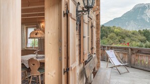 A wooden cabin with a dining area, a table with a lamp, and a view of mountains. - Ötztal Chalet (Sautens)
