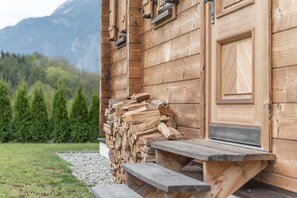 A wooden cabin with a wooden staircase leading to a door, a stack of firewood, and a view of a forest and mountains in the background. - Ötztal Chalet (Sautens)