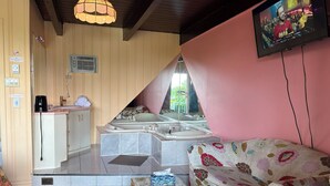 Una habitación con kitchenette, un ventanal grande, un sofá y televisión.