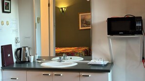Un baño de hotel con lavabo, espejo y un microondas en un estante.