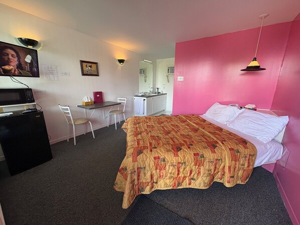 Una habitación con cama, escritorio, silla, microondas y refrigerador.