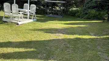 A grassy outdoor area with two white metal picnic tables and chairs, surrounded by trees and a utility pole.