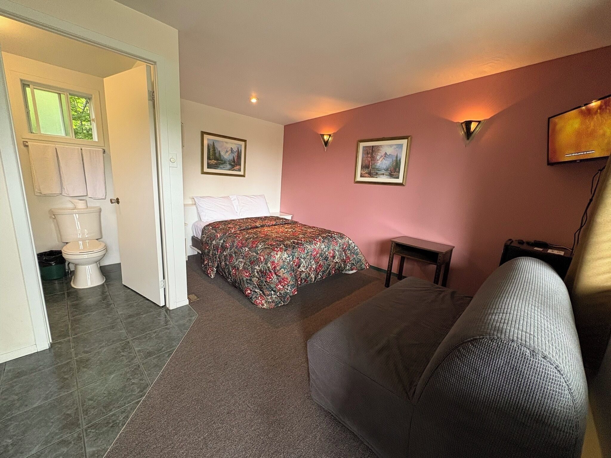 A bedroom with a bed, a sofa, a small table, and a painting on the wall.