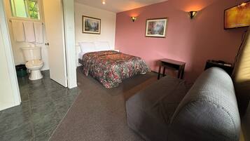 A bedroom with a bed, a sofa, a small table, and a painting on the wall.