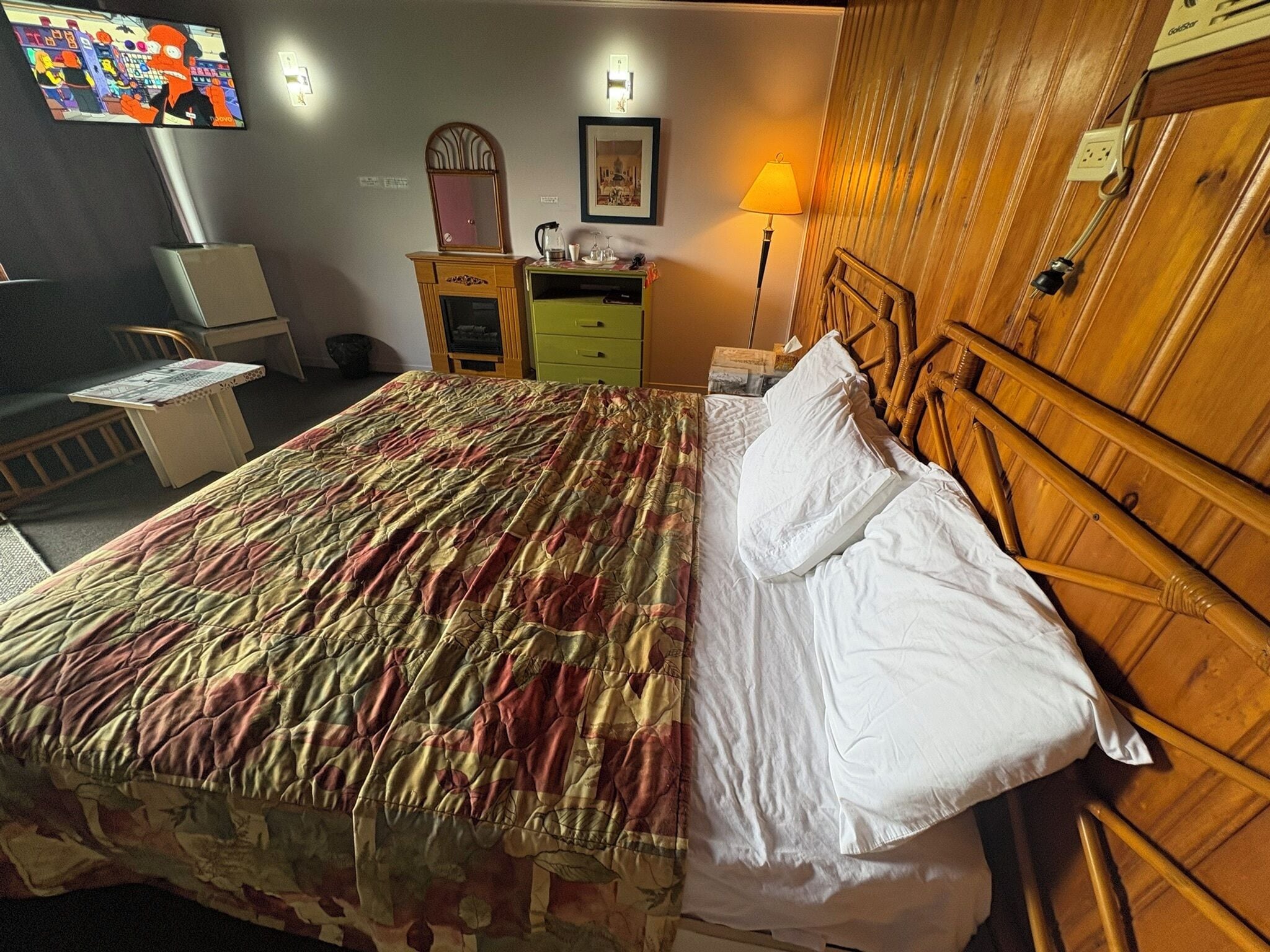 Een hotelkamer met een bed, een bureau, een stoel, een lamp en een televisie aan de muur.