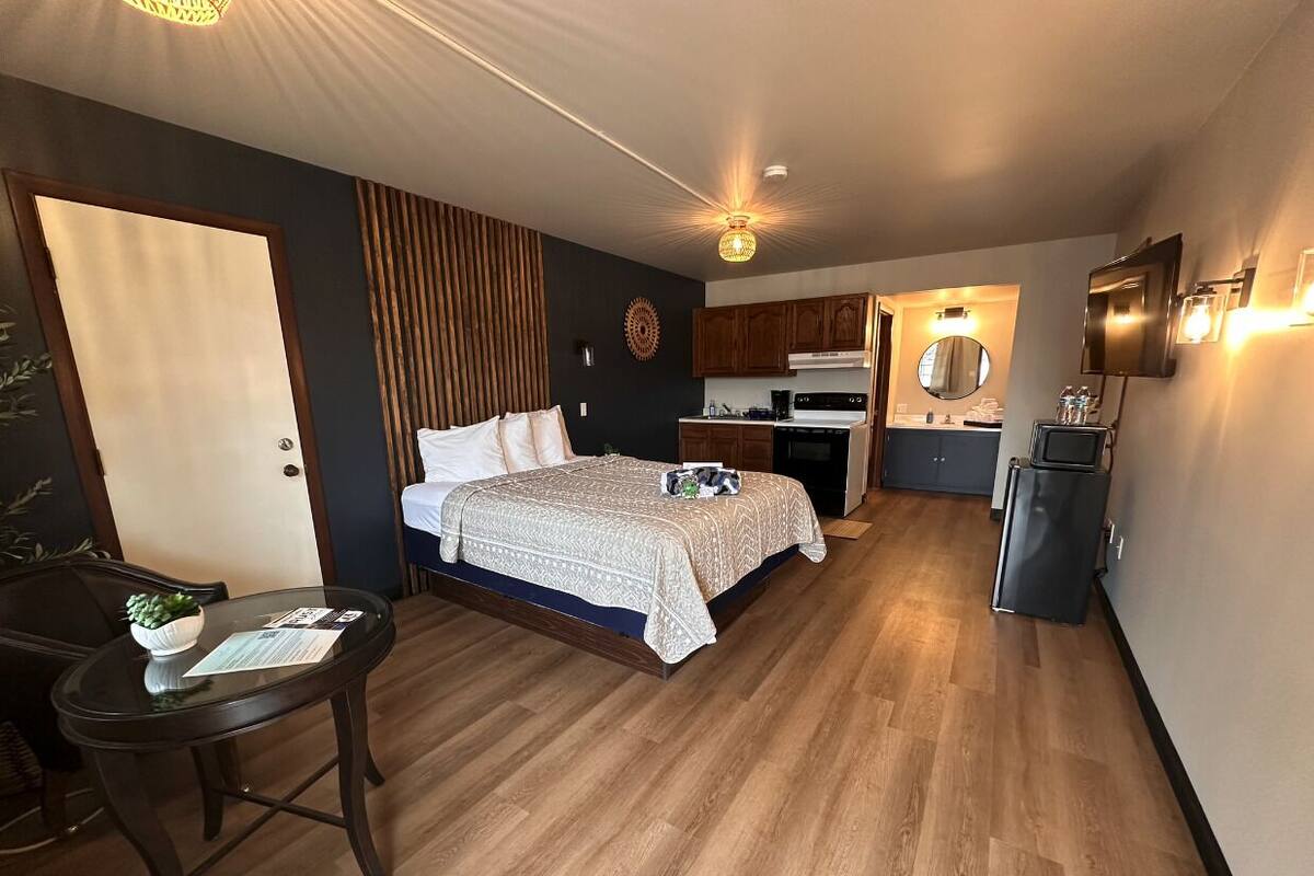 Een compacte hotelkamer met een bed, een klein bureau, een kitchenette en een badkamer.