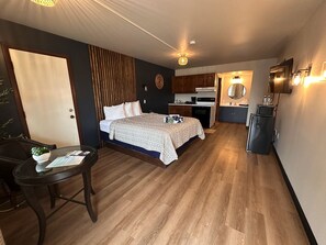 A compact hotel room with a bed, a small desk, a kitchenette, and a bathroom.