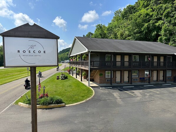 A motel with a two-story building, a covered porch, and a parking lot. - The Roscoe (Coshocton)