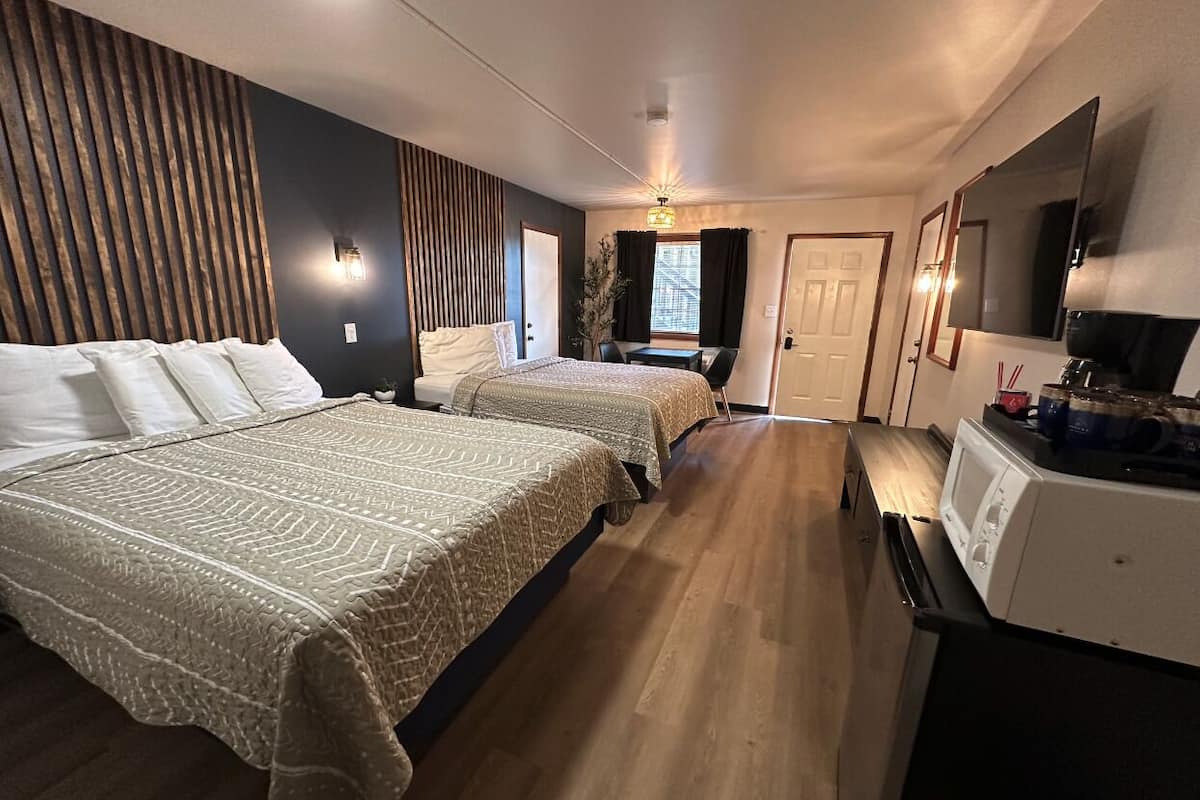 Een hotelkamer met twee bedden, een kitchenette, een televisie en een raam met gordijnen.