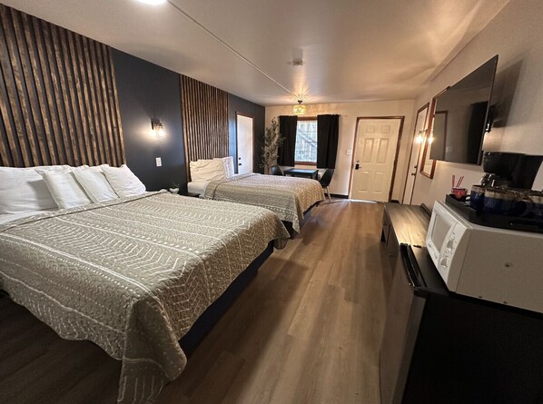 A hotel room with two beds, a kitchenette, a seating area with a table and chairs, and a large mirror. - The Roscoe (Coshocton)