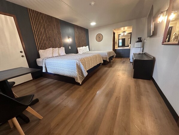 A hotel room with two beds, a desk, a chair, a small kitchenette, and a mirror. - The Roscoe (Coshocton)