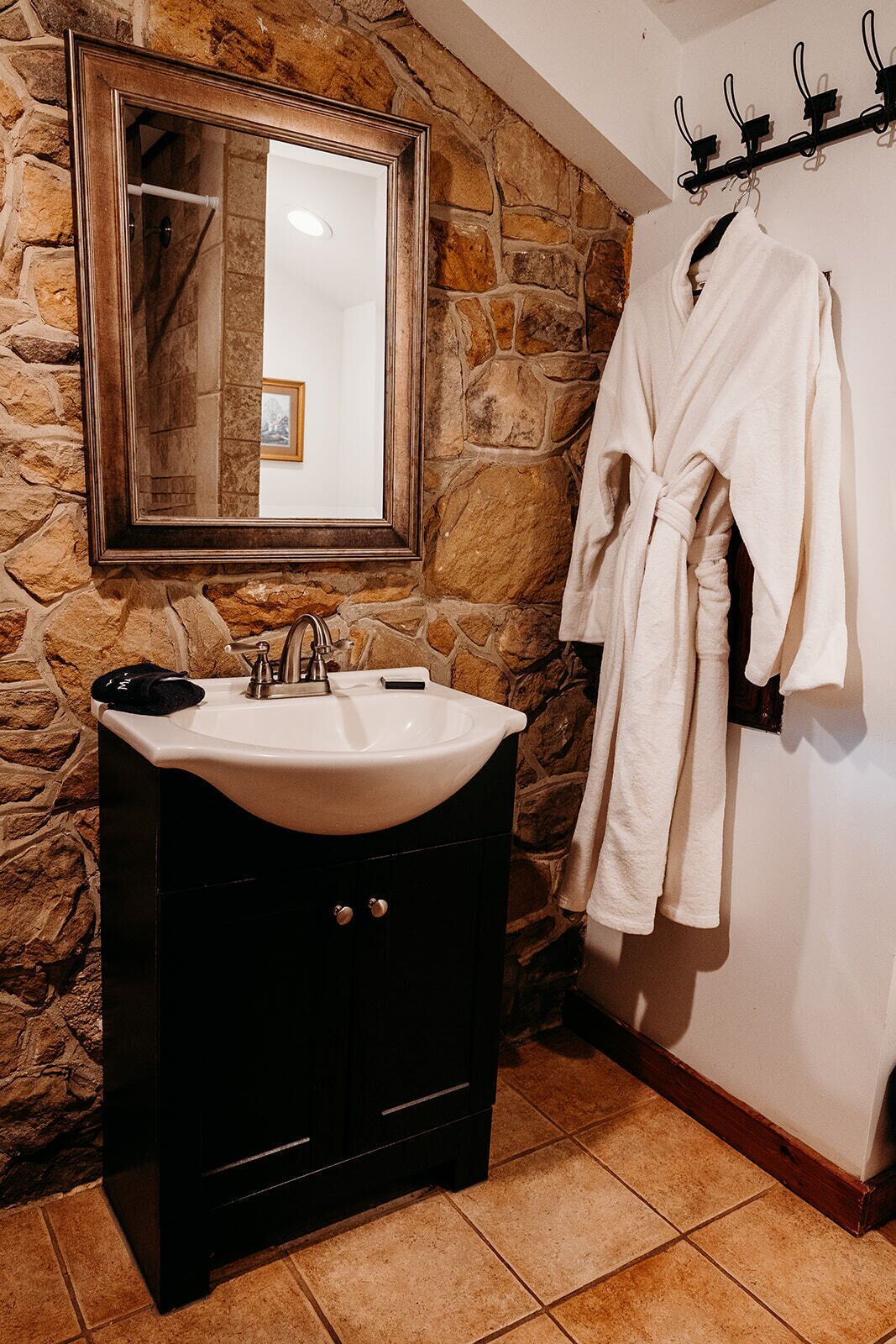 A bathroom with a stone wall, a sink with a mirror, and a robe hanging on a rack.