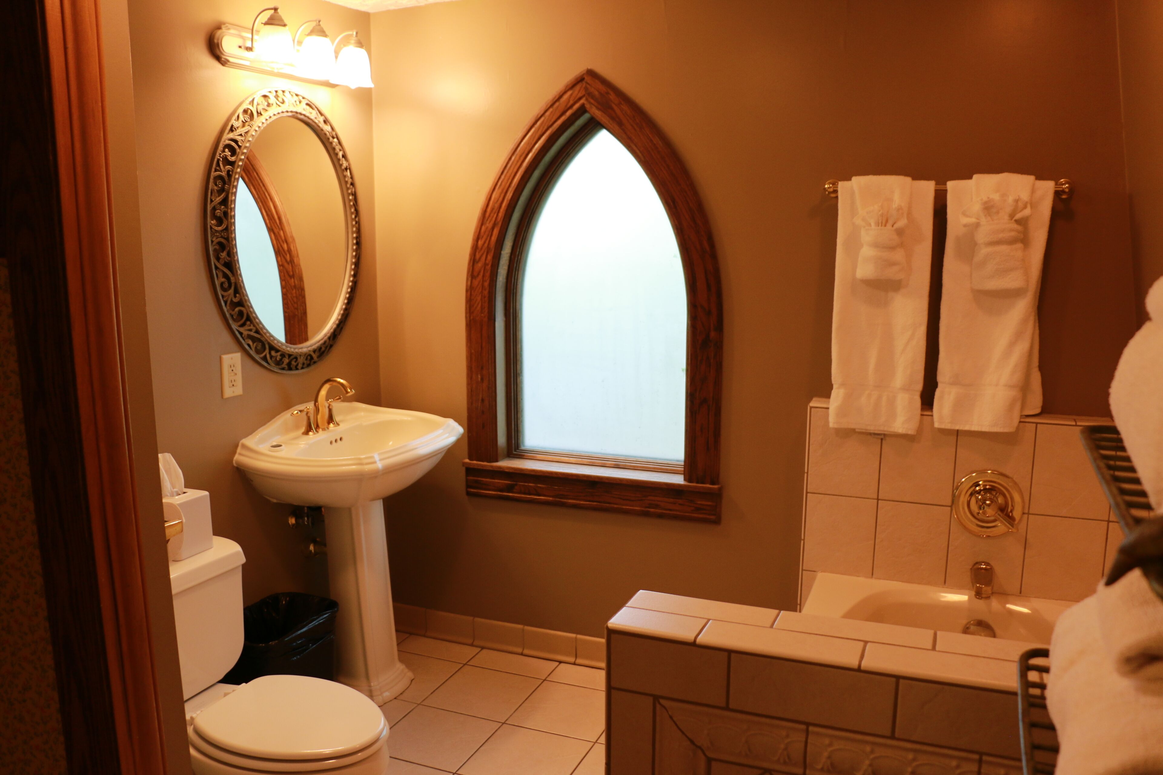 A bathroom with a white sink, a toilet, a vanity with a mirror, and a window.