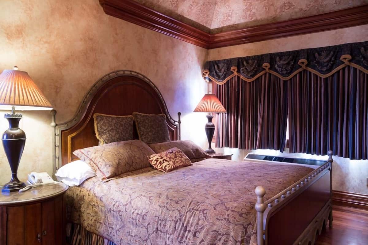 A classic four-poster bed with a wooden frame and ornate headboard, flanked by two bedside tables with lamps.