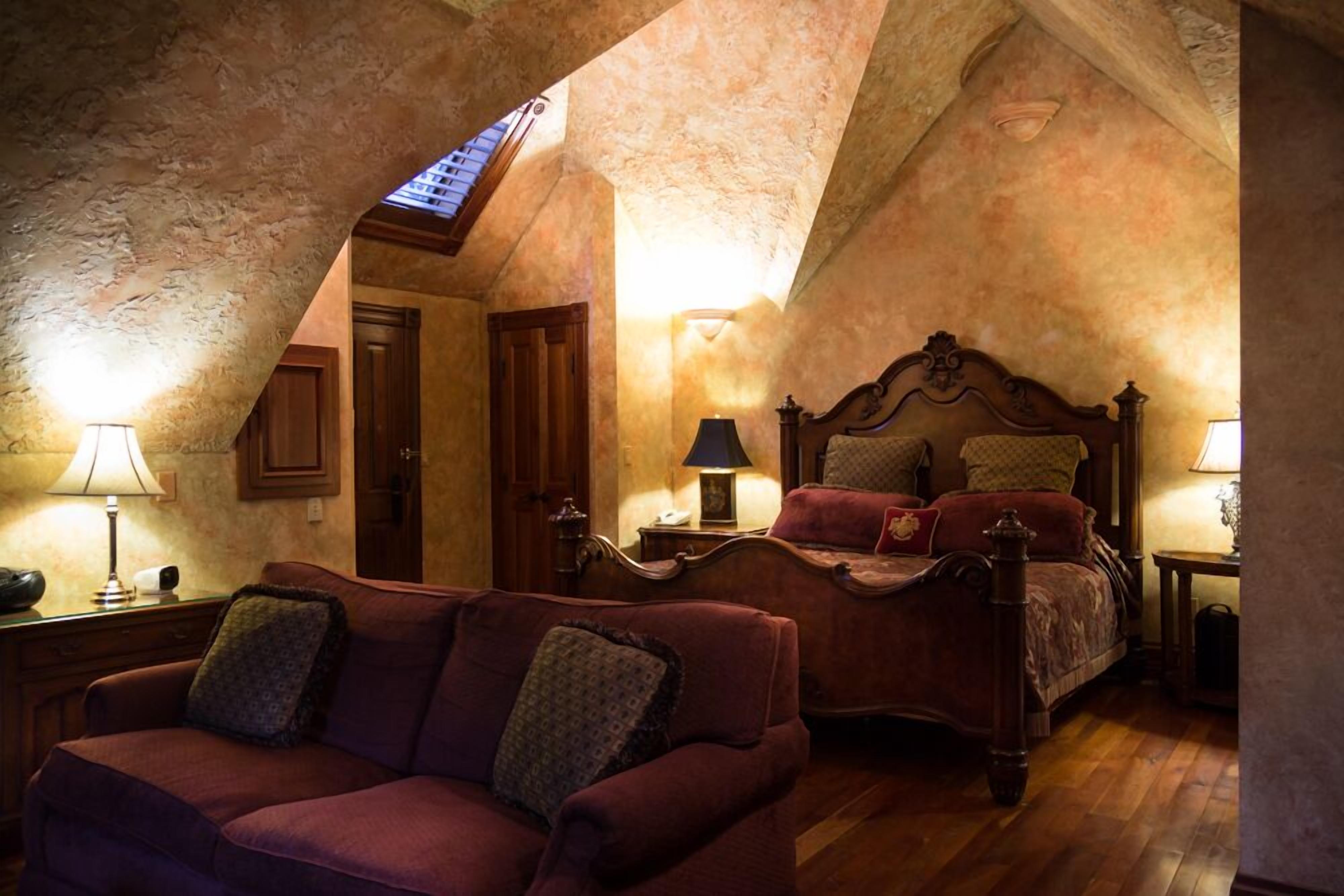 A bedroom with a sloped ceiling, a wooden bed, a red sofa, and two bedside lamps.