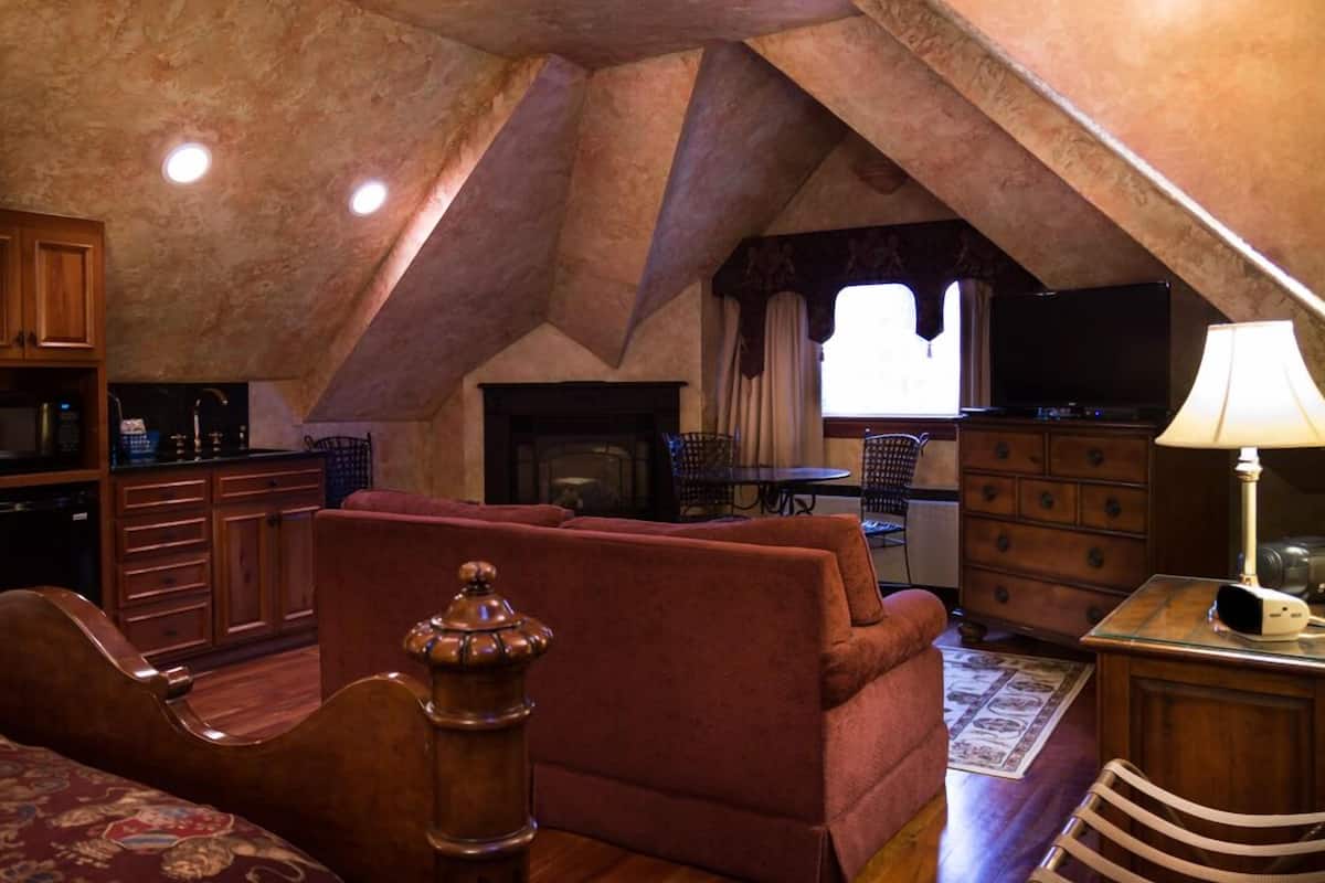 A cozy attic room with a fireplace, a sofa, a TV, and wooden cabinets.