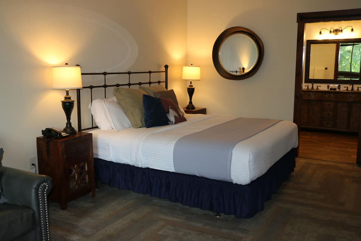 A neatly made bed with a headboard, two bedside lamps, a nightstand with a phone, and a mirror above the bed.