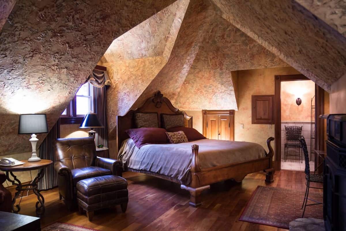 A bedroom with a wooden bed, leather armchair, and a small table with a lamp.