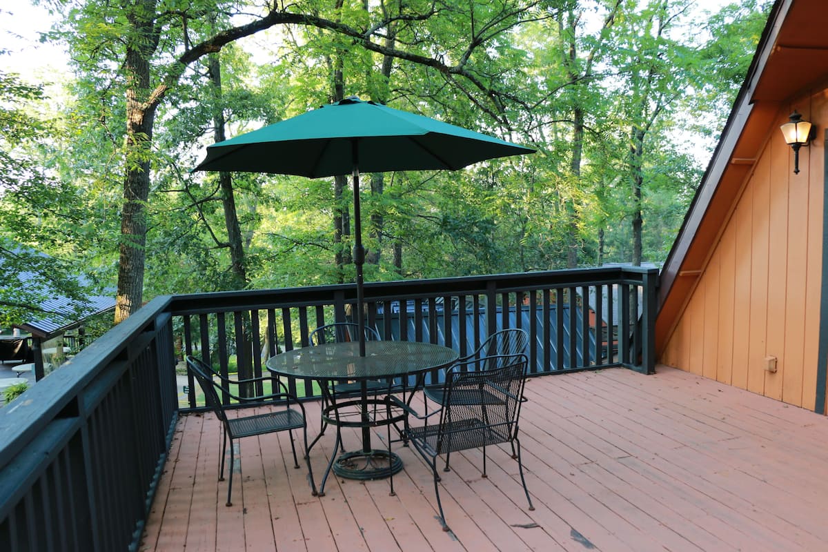 A wooden deck with a round table and chairs, surrounded by a black railing.