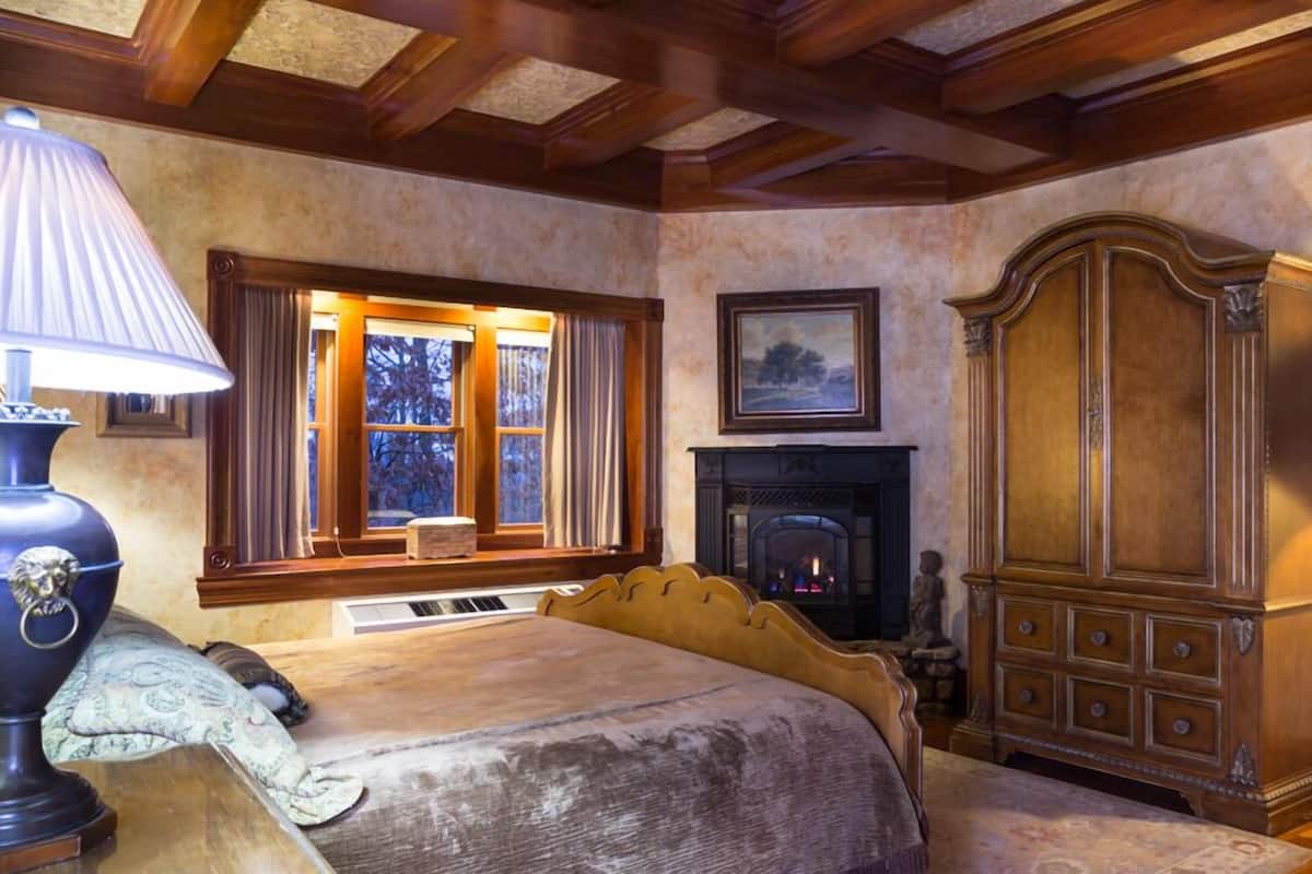 A bedroom with a bed, a fireplace, a large wooden armoire, and a window with curtains.