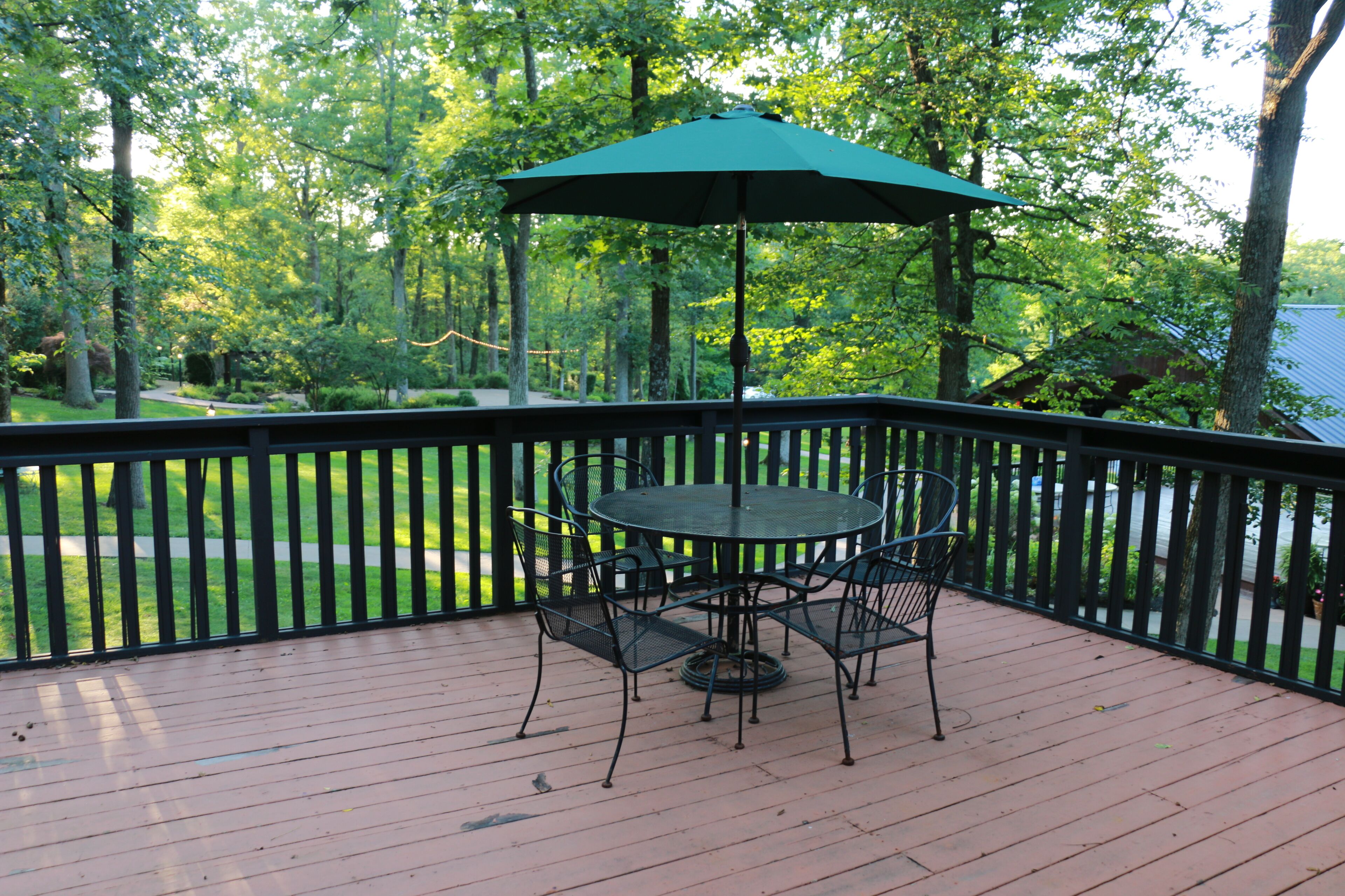 A wooden deck with a round table and chairs, surrounded by a black railing.